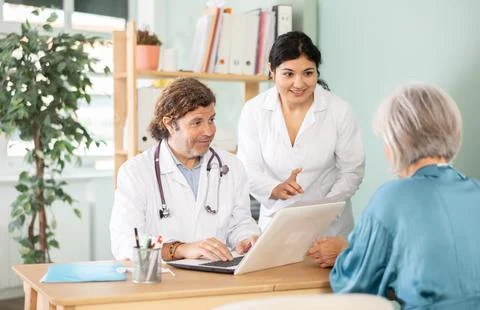 Two doctors talking with elderly patient at table in medical office Stock Photos