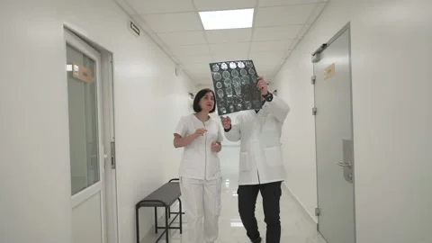 Two doctors walk down corridor and discussing about mri brain scan. Healthcare Stock Footage 166460173