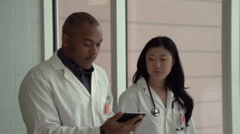 Two doctors walking and talking with their tablet Stock Footage 24631695
