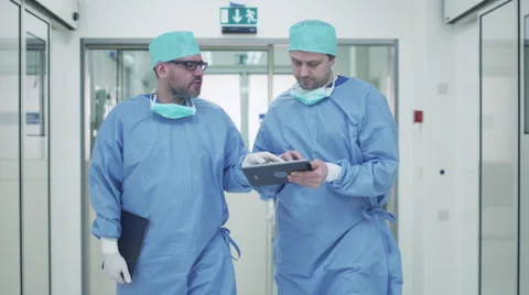Two Doctors Walking through Hospital and Chatting. Holding Tablet in Hands. Stock Footage