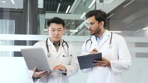 Two doctors in white coats collaborate over a laptop and folder standing  Stock Footage 302893742