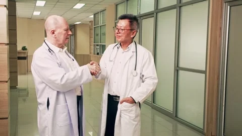 Two doctors in white coats shake hands in hospital corridor, showing physician Stock Footage 315160188