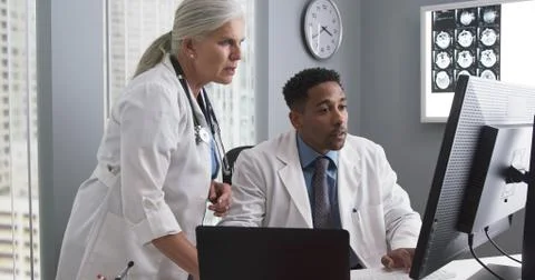 Two doctors working inside medical office looking at computer monitor and typ Stock-Fotos