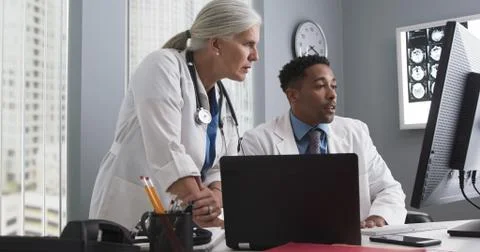 Two doctors working inside medical office looking at computer monitor and typ Stock-Fotos