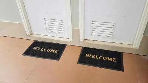 Two doormats lying in front of two doors with welcome written on it Stock Photos