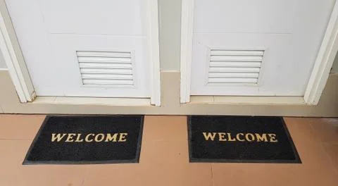 Two doormats lying in front of two doors with welcome written on it Stock Photos