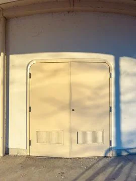 Two doors are set in a light wall. The sun is low, making long shadows on the Stock Photos