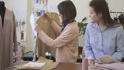 Two dressmakers are looking at clothes, standing in sewing studio, young women Stock Footage 88483982