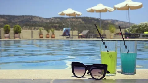 Two drinks and sunglasses by a poolside on a sunny day with mountains Stock Footage 328672433