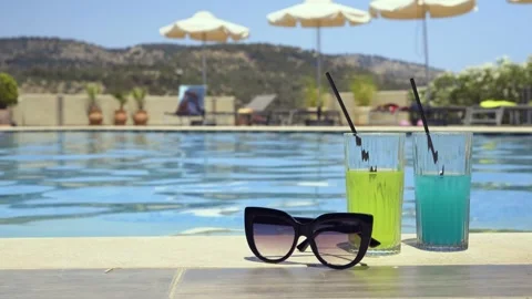Two drinks and sunglasses by a poolside on a sunny day, space for text, Greece Stock Footage 328672740