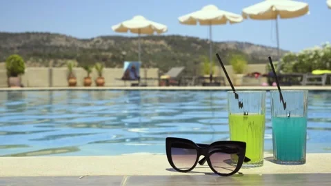 Two drinks and sunglasses by a poolside on a sunny day, summer vibe Stock Footage 328673548