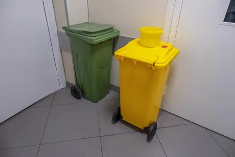 Two dumpsters of different colors are in the corner of the room Stock Photos