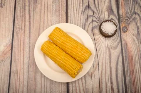 Two ears of boiled corn in a plate and coarse salt on the table. Healthy diet Stock Photos