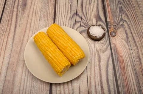 Two ears of boiled corn in a plate and coarse salt on the table. Healthy diet Stock Photos