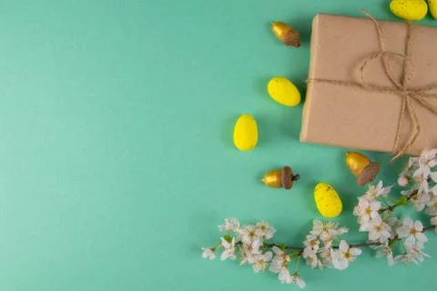 Two easter gifts, yellow eggs and white spring flowers on a mint background c 库存照片