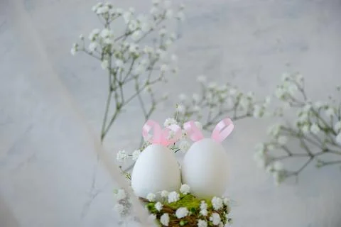 Two Easter white eggs with pink ears made of ribbons in a green nest around w Stock Photos