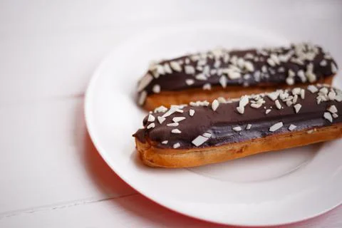 Two eclairs on a white plate on a light wooden background Stock Photos