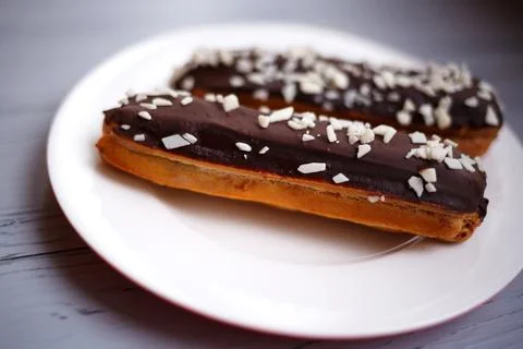 Two eclairs on a white plate on a light wooden background Stock Photos
