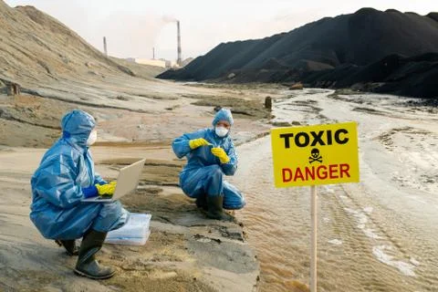 Two ecologists in protective coveralls studying characteristics of toxic water Fotos de archivo