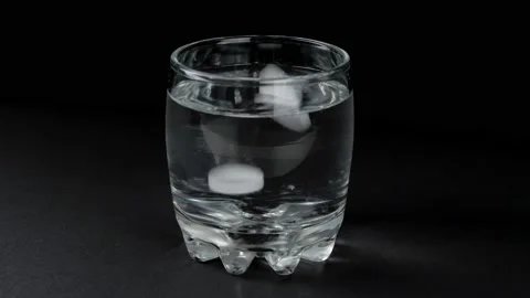 Two effervescent tablets dissolved in a glass of water. Black background. Видео 132750574