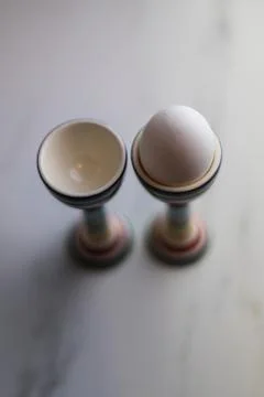 Two eggcups on a marble table with colorful stripes and only one egg Stock Photos