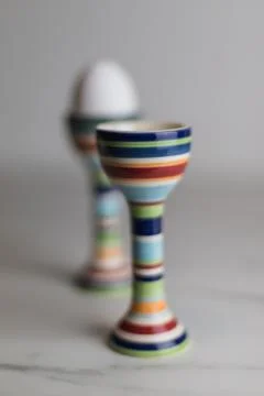 Two eggcups on a marble table with colorful stripes and only one egg Stock Photos