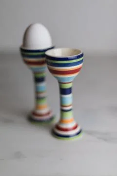 Two eggcups on a marble table with colorful stripes and only one egg Stock Photos