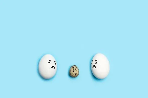 Two eggs with angry face looking at a quail egg on a blue background Foto stock