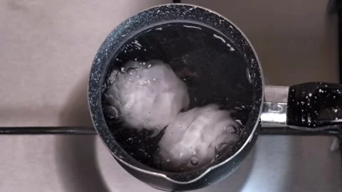 Two eggs are boiled in boiling water on a gas gray stove in the kitchen close-up Stock Footage 248893649