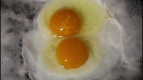 Two eggs are expertly cracked open into a hot skillet, revealing bright, golden Stock Footage 292754512