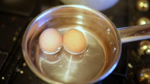 Two eggs boiling in hot water in a cooking pot on gas stove Stock Footage 317102635