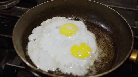 Two eggs frying in a pan on a stovetop, close-up shot Stock Footage 342637341