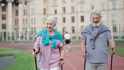 Two elder people nordic walking poles sport hiking park. Old love couple smiling Stock Footage 231177369