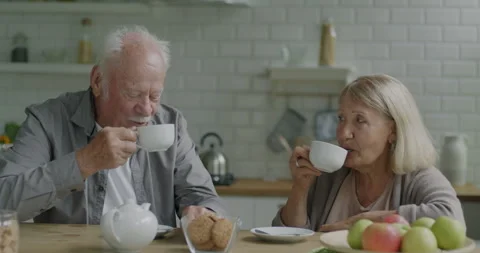 Two elderly people man and woman drinking coffee clinking cups and talking at Stock Footage
