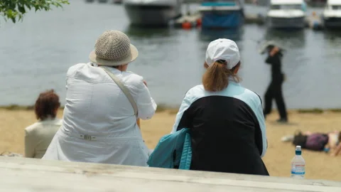 Two elderly women are sitting on a bench by the sea, gazing at the water. A.. 動画素材 344464106