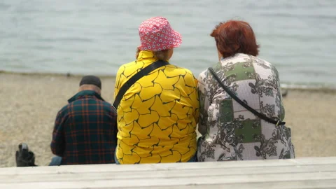 Two elderly women are sitting on a bench by the sea, gazing at the water. A.. 動画素材 344512222