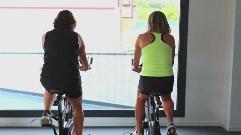 Two Elderly women seen from behind doing cardio exercise on spin bikes at gym Stock Footage 285092338