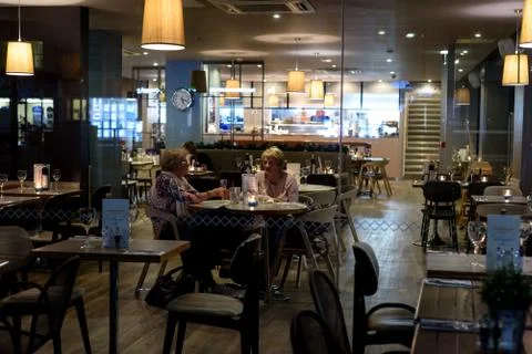 Two elderly women sit at a table of a restaurant cafe bar at night in Chelmsf Stock Photos