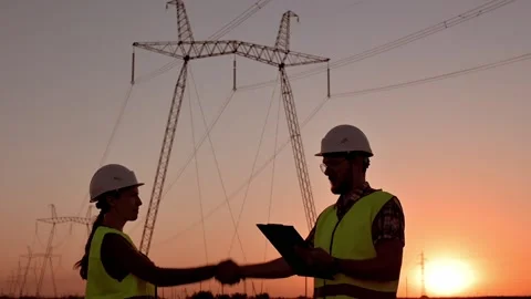 Two electrical engineers meet and shake hands against the backdrop of high Stockbeeldmateriaal 204857743