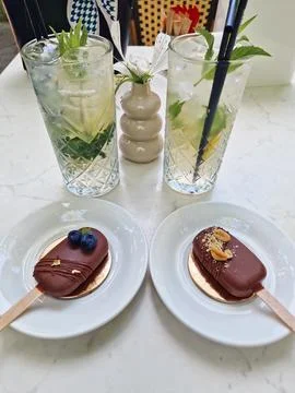 Two elegant chocolate popsicle cakes sit on the table near tall glasses of .. Stock-Fotos
