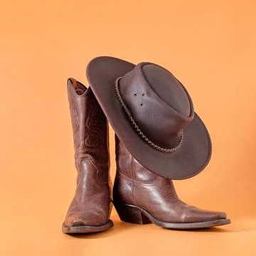 Two elegant classic boots and a leather cowboy stetson hat on an orange clay  Foto stock