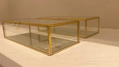 Two elegant glass boxes with gold frames on a light surface, slow motion Stock Footage 308167070
