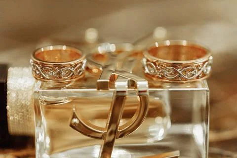 Two elegant gold wedding rings with intricate knot designs resting on a clear Stock Photos
