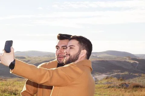 Two elegant men in nature taking a selfie photo with smart phone. gay couple Foto stock