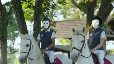 Two elegant people wearing anonymous masks riding white horses at sunset Vídeo Stock 98437883