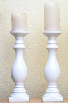 Two elegant white ceramic candle holders with faux candles on a textured wa.. Stock Photos