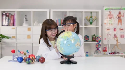 Two Elementary School Girls in Lab Coats Studying a World Globe Stock Footage 341917412