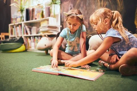 Two elementary schoolgirls solving puzzles and riddles in school library. S.. Stock Photos