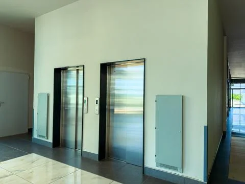 Two elevators are installed in a hallway of a modern building. The area has w Stock Photos