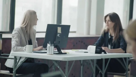 Two employees girlfriends are sitting at the same desk, chatting and smiling Stock Footage 124269698